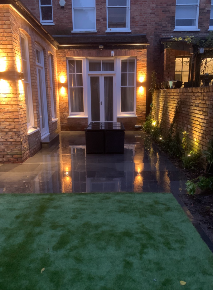 A well-lit patio with dark furniture, polished flooring, and greenery.