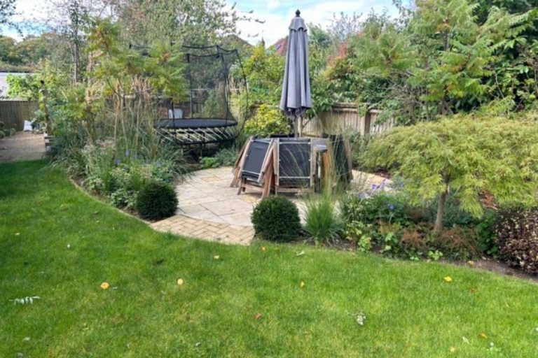 A landscaped garden featuring a patio, seating area, and greenery.