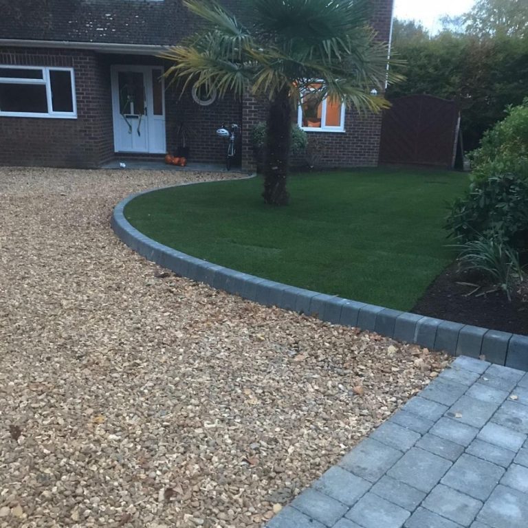 Pathway bordered by stones, leading to a house and landscaped garden with a palm tree.