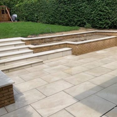 Paved garden area with steps and raised planting beds, surrounded by greenery.
