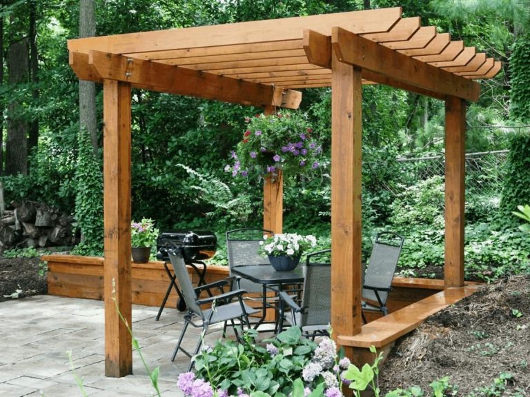 Wooden pergola with seating area and plants in a landscaped garden.