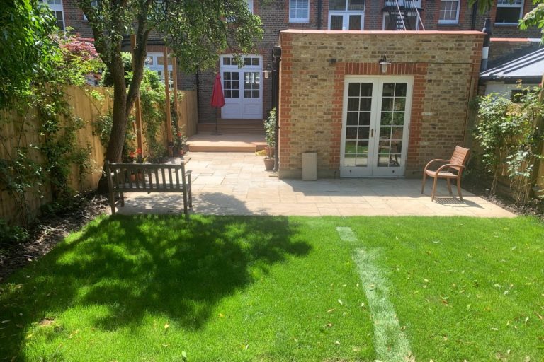 A well-maintained garden with green grass, stone patio, and wooden benches.