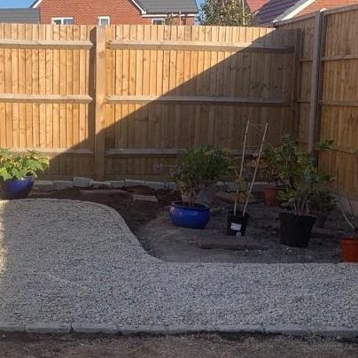 A tidy garden with gravel pathways and potted plants near a wooden fence.