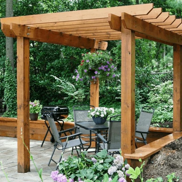 Wooden pergola with seating area and potted plants in a lush garden setting.