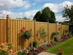 Wooden garden fence with hanging plants and flowers, under a partly cloudy sky.