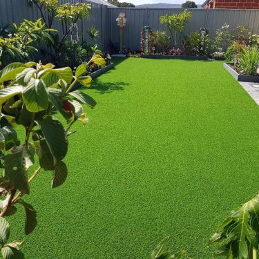 Vibrant green artificial lawn surrounded by plants and garden features.