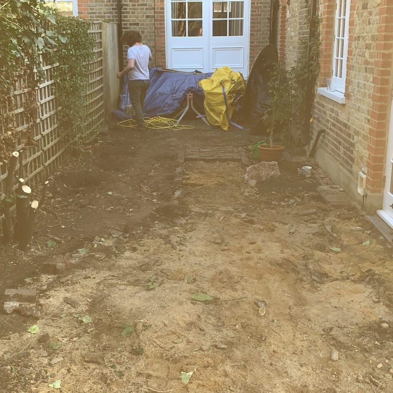 A person working in a garden, clearing soil near a yellow and blue tarpaulin.