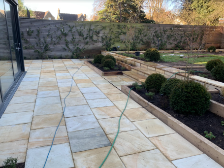 Paved patio area with landscaped garden beds and neatly trimmed hedges.