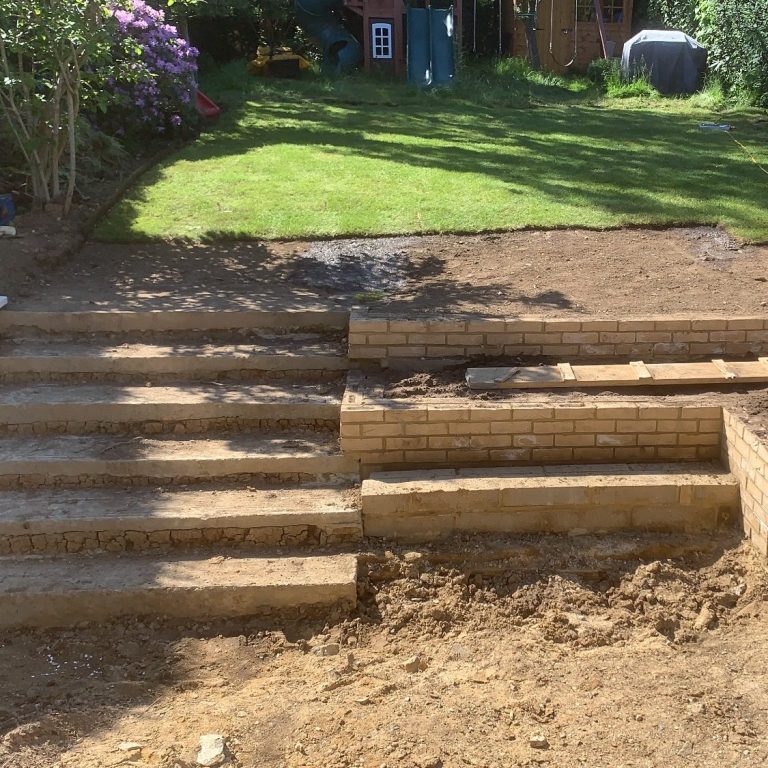Garden area with wooden steps leading up a grassy slope, surrounded by plants.